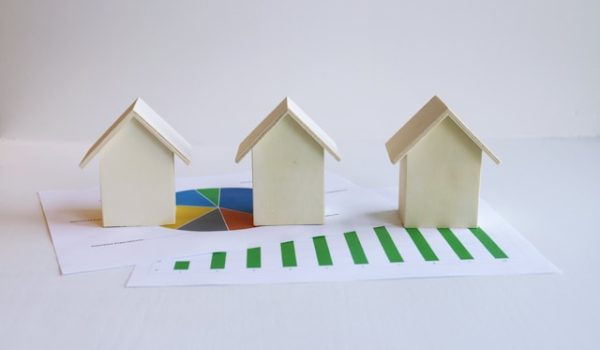 A image of three paper houses on top of a paper with mortgage data charts, symbolizing the mortgage market.