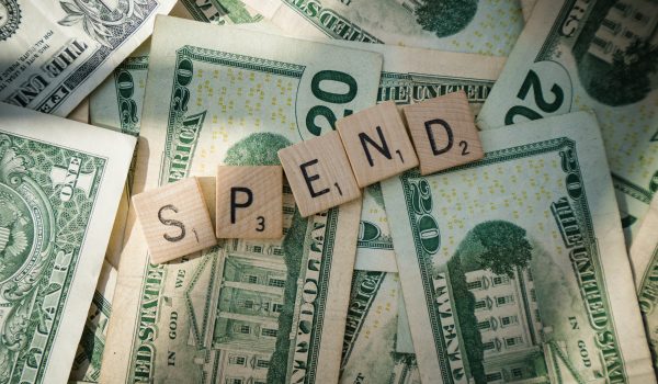 Scrabble letters spelling 'spend' on American bills, sinifying the consumer financial trends.